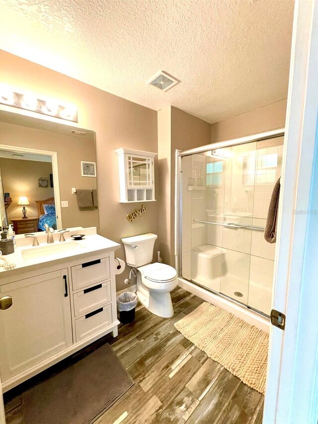 bathroom featuring a textured ceiling, hardwood / wood-style flooring, toilet, and an enclosed shower