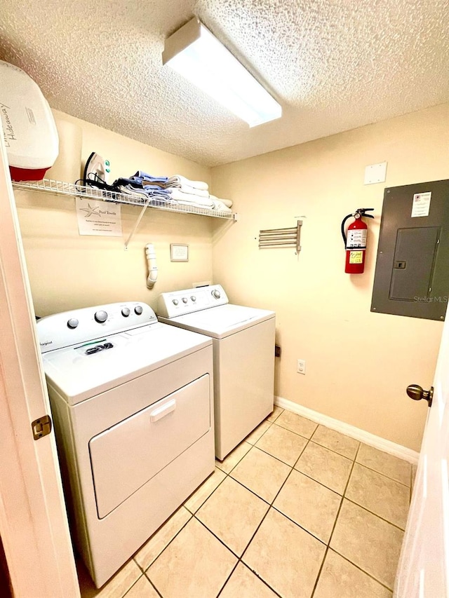 clothes washing area with electric panel, light tile patterned flooring, washer and dryer, and a textured ceiling