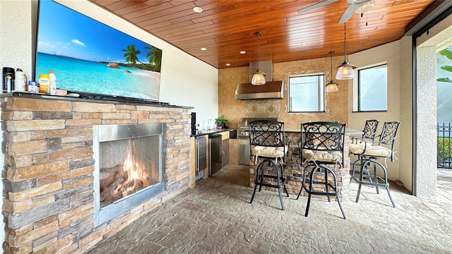 interior space featuring an outdoor stone fireplace, ceiling fan, wall chimney range hood, hanging light fixtures, and wood ceiling