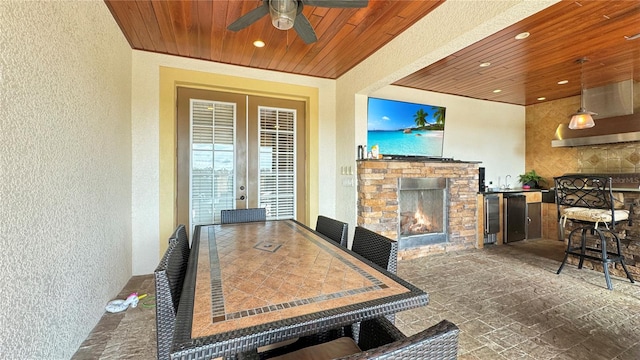 interior space with a stone fireplace, ceiling fan, wood ceiling, french doors, and dark tile flooring