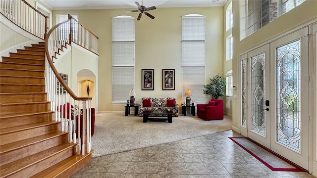 interior space with a towering ceiling, ceiling fan, light tile flooring, french doors, and ornamental molding