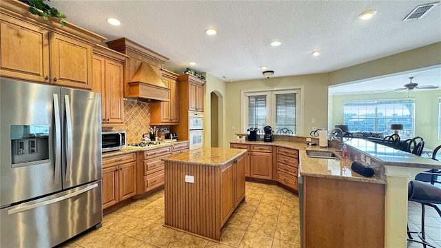 kitchen with appliances with stainless steel finishes, a kitchen breakfast bar, ceiling fan, a kitchen island, and light stone counters