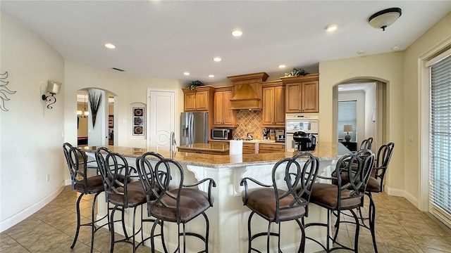 kitchen with a breakfast bar, appliances with stainless steel finishes, premium range hood, and light tile floors