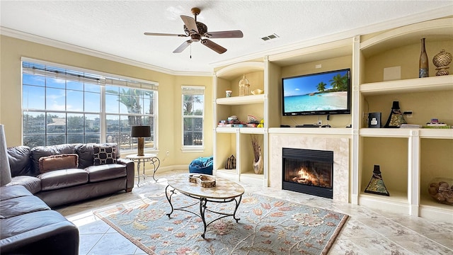 living room with light tile floors, built in shelves, ceiling fan, a fireplace, and a textured ceiling