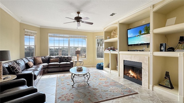 tiled living room featuring a tile fireplace, built in features, ceiling fan, a textured ceiling, and ornamental molding