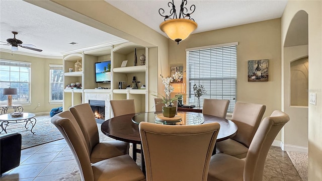 dining room with light tile flooring, a fireplace, ceiling fan, a textured ceiling, and built in shelves