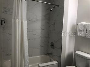 bathroom with shower / bathtub combination with curtain and toilet