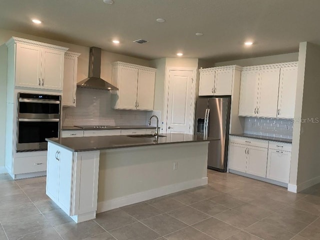 kitchen with dark countertops, visible vents, wall chimney range hood, stainless steel appliances, and a sink