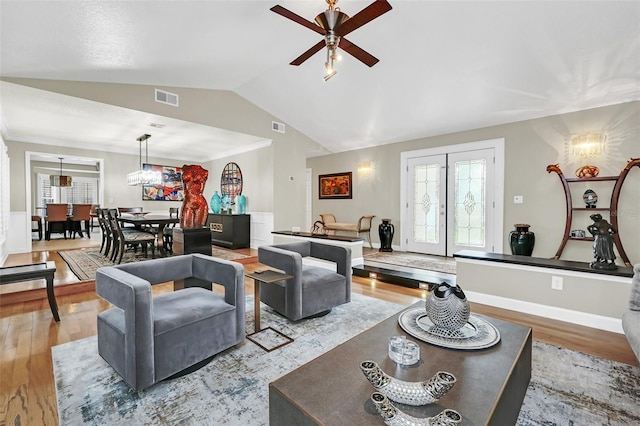 living room featuring vaulted ceiling, light hardwood / wood-style floors, french doors, and ceiling fan with notable chandelier