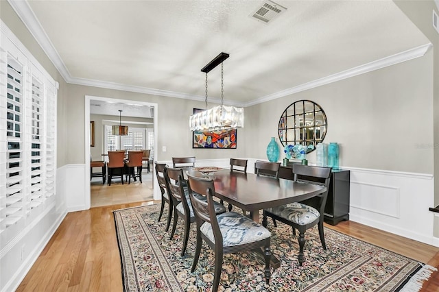 dining room with light hardwood / wood-style floors, a notable chandelier, a textured ceiling, and crown molding