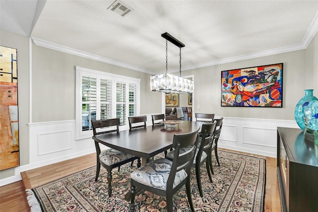 dining room with ornamental molding, a textured ceiling, a chandelier, and light hardwood / wood-style flooring