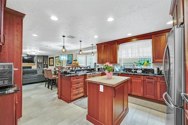 kitchen featuring kitchen peninsula, stainless steel fridge, light tile floors, decorative light fixtures, and a center island