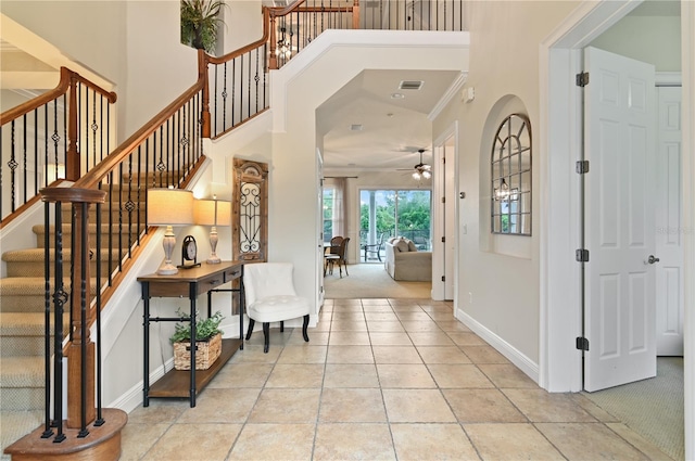 carpeted foyer entrance with ceiling fan, a towering ceiling, and ornamental molding