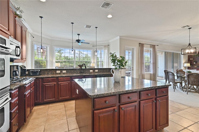 kitchen featuring appliances with stainless steel finishes, a kitchen island, ceiling fan with notable chandelier, and hanging light fixtures