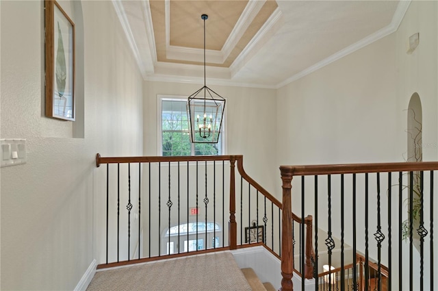 corridor featuring a notable chandelier, a tray ceiling, and ornamental molding