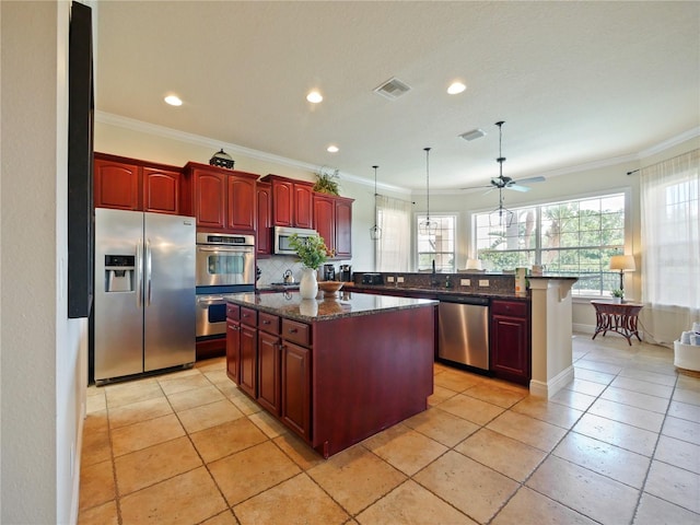 kitchen featuring ceiling fan, appliances with stainless steel finishes, dark stone counters, hanging light fixtures, and a center island