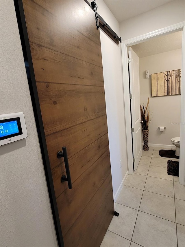 hall featuring light tile patterned floors, baseboards, and a barn door