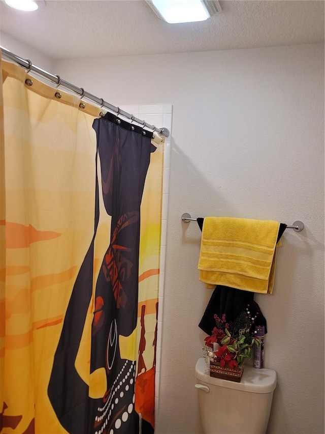 bathroom featuring a textured ceiling, toilet, and a shower with shower curtain