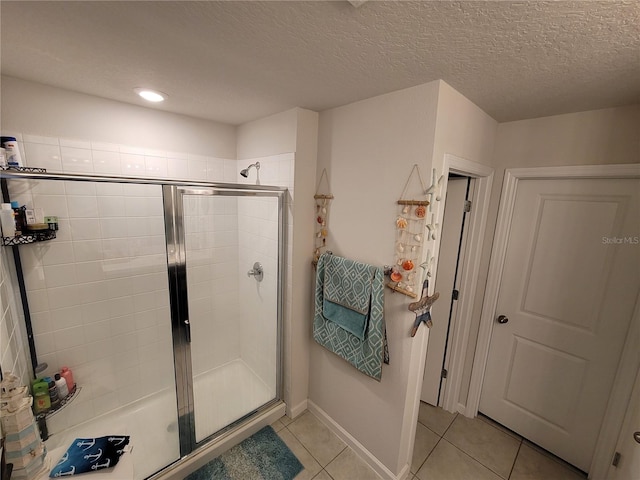 bathroom with tile patterned floors, a shower stall, a textured ceiling, and baseboards