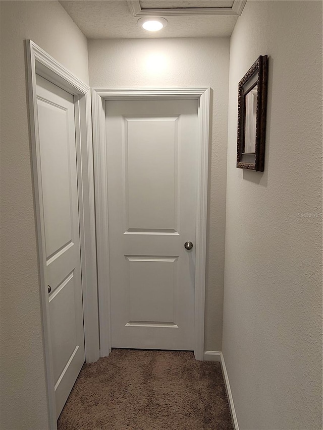 hallway featuring baseboards, attic access, a textured wall, and carpet floors