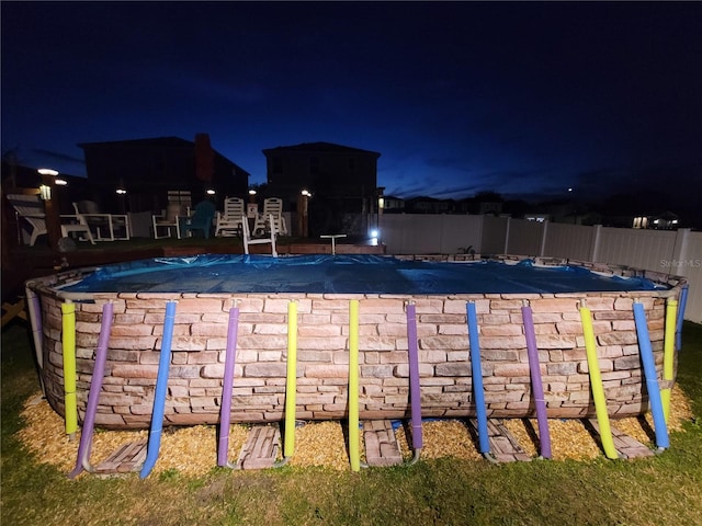 pool at night featuring a community pool and fence