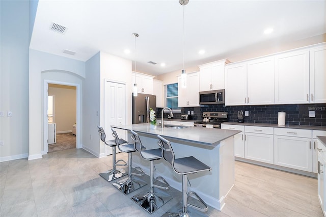 kitchen featuring an island with sink, pendant lighting, stainless steel appliances, white cabinets, and sink