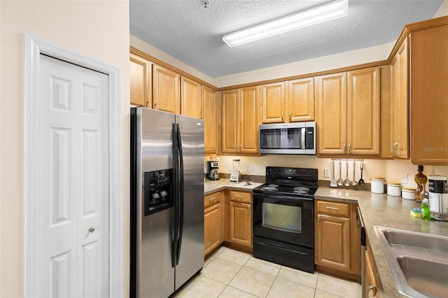 kitchen featuring light tile flooring, a textured ceiling, appliances with stainless steel finishes, and sink