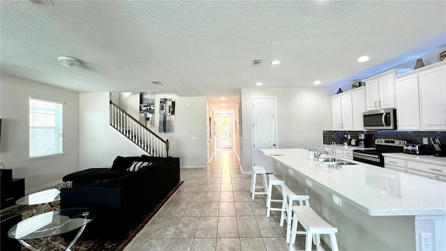 kitchen featuring stainless steel appliances, tasteful backsplash, white cabinetry, a kitchen breakfast bar, and sink