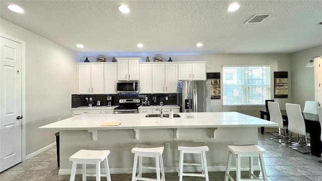 kitchen with appliances with stainless steel finishes, light tile floors, tasteful backsplash, a breakfast bar area, and a kitchen island with sink