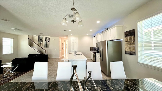 kitchen featuring light tile floors, a notable chandelier, white cabinetry, stainless steel appliances, and pendant lighting