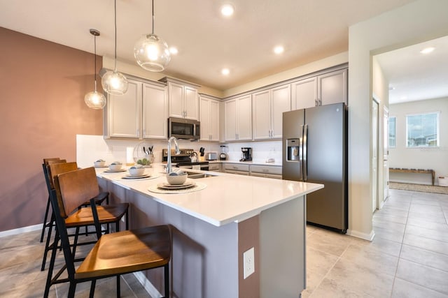 kitchen with a breakfast bar, sink, stainless steel appliances, light tile floors, and pendant lighting