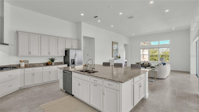 kitchen with stainless steel appliances, a center island with sink, sink, light stone countertops, and white cabinets