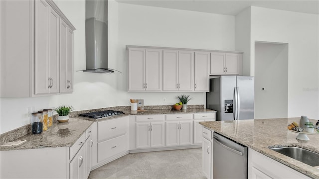 kitchen with wall chimney range hood, white cabinets, light stone counters, sink, and stainless steel appliances