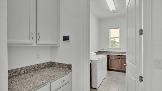 laundry area featuring washer and dryer, light tile patterned floors, and cabinets