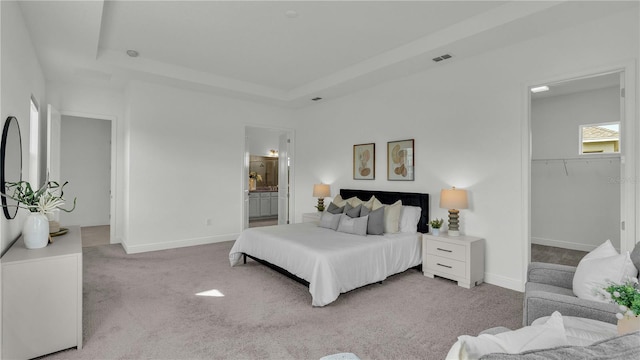 carpeted bedroom with a spacious closet, a closet, ensuite bathroom, and a raised ceiling