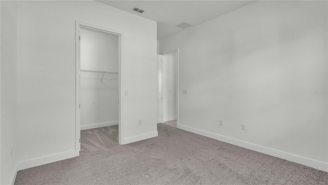 unfurnished bedroom featuring a walk in closet, a closet, and light colored carpet