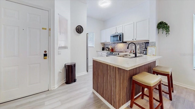 kitchen with light wood-type flooring, white cabinetry, appliances with stainless steel finishes, sink, and a breakfast bar area