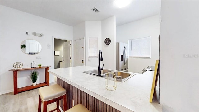 kitchen with sink, light hardwood / wood-style flooring, stainless steel fridge, and a breakfast bar area