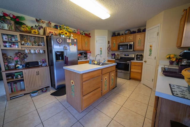 kitchen featuring appliances with stainless steel finishes, a center island with sink, light tile floors, a textured ceiling, and sink