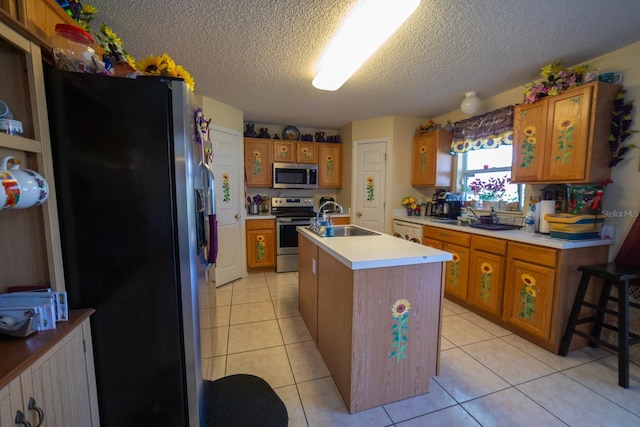 kitchen with an island with sink, stainless steel appliances, sink, and light tile floors