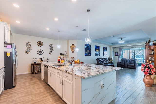 kitchen with a kitchen island with sink, pendant lighting, white cabinets, light hardwood / wood-style flooring, and stainless steel appliances