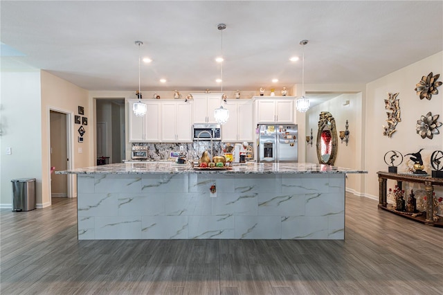 kitchen with light stone countertops, hanging light fixtures, stainless steel appliances, white cabinets, and dark hardwood / wood-style flooring