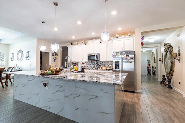 kitchen featuring an island with sink, stainless steel appliances, decorative light fixtures, white cabinets, and dark hardwood / wood-style floors