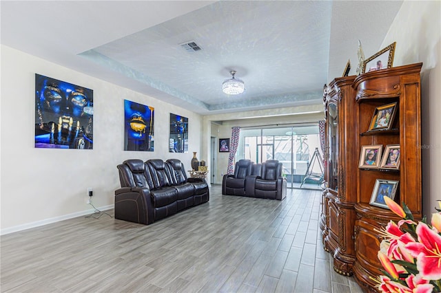 living room with a raised ceiling, light hardwood / wood-style floors, and a textured ceiling