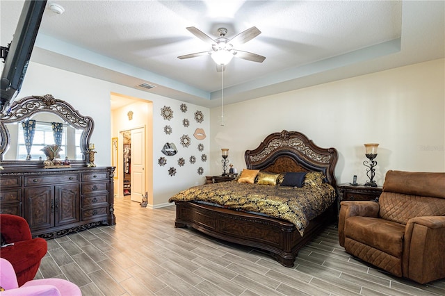 bedroom featuring ceiling fan, a textured ceiling, a closet, a raised ceiling, and light wood-type flooring