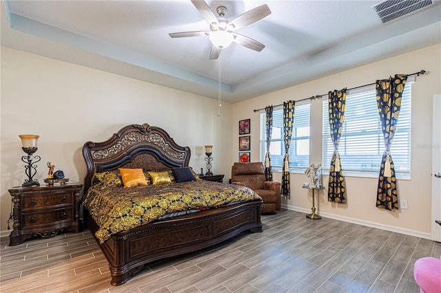 bedroom featuring a tray ceiling, ceiling fan, and light wood-type flooring