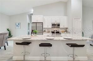 kitchen featuring white cabinets, a breakfast bar area, stainless steel appliances, and lofted ceiling