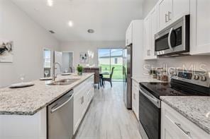 kitchen featuring an island with sink, light stone countertops, appliances with stainless steel finishes, white cabinets, and light wood-type flooring