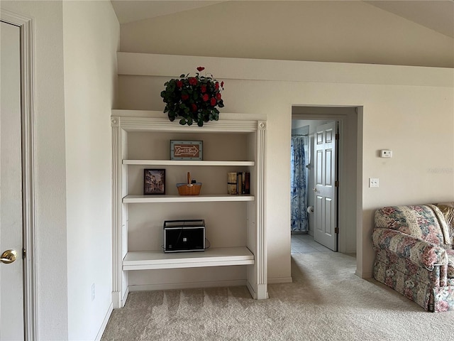 hallway featuring lofted ceiling, built in features, and light carpet