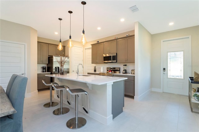 kitchen featuring a kitchen island with sink, sink, a kitchen breakfast bar, appliances with stainless steel finishes, and decorative light fixtures